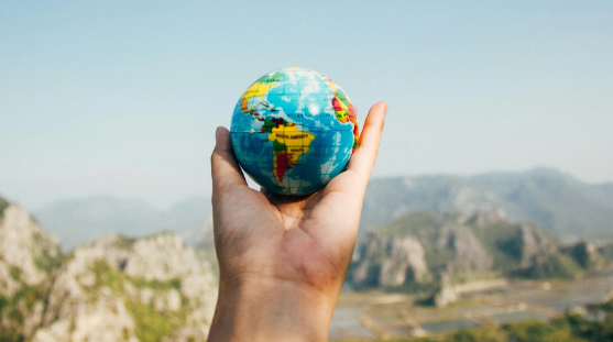 Hand holding a small globe with a mountainous landscape in the background, used in a geography quiz created with Opinion Stage.